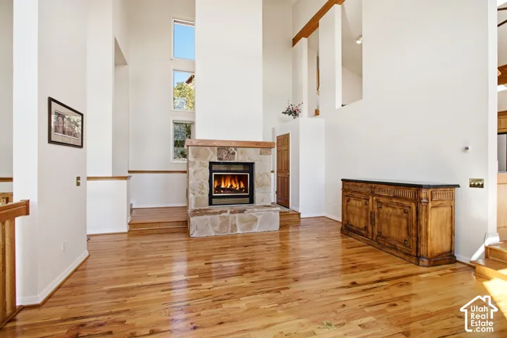Hardwood flooring throughout, stone-clad fireplace with wood mantel, vaulted ceiling, multiple windows, and wood-finish banister