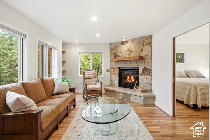 Stone-clad fireplace with a wood mantle, recessed lighting, wood-finish flooring, and multiple windows