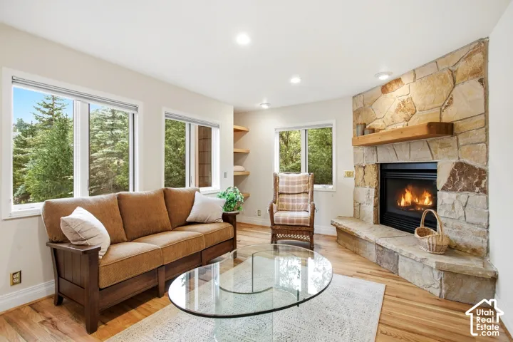 Hardwood-style flooring, stone-clad corner fireplace with wood mantel, built-in corner shelving, recessed lighting, and multiple windows