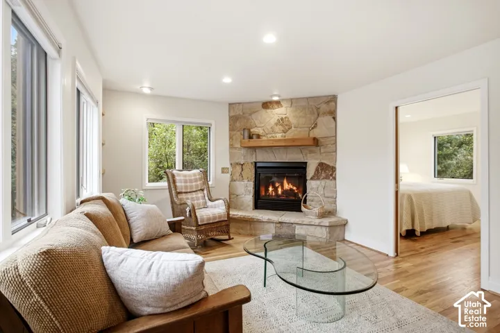 Corner stone fireplace with wood mantel, recessed lighting, wood-finish flooring, and multiple windows