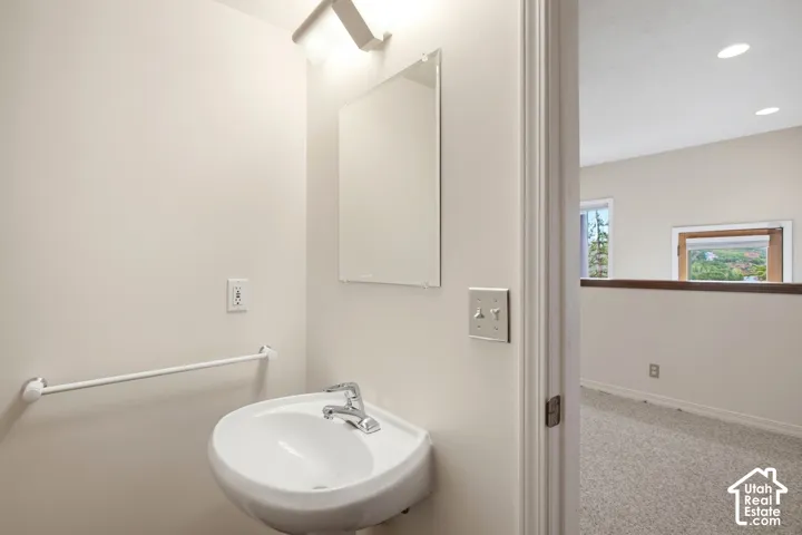 Wall-mounted pedestal sink with chrome faucet, vanity mirror, and overhead lighting fixture