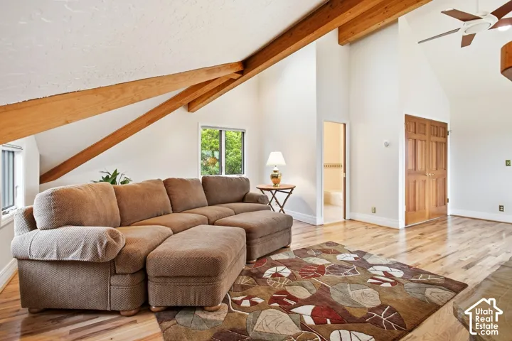 Vaulted ceiling with exposed wood beams, wood-finish flooring, operable windows, and an attached ceiling fan