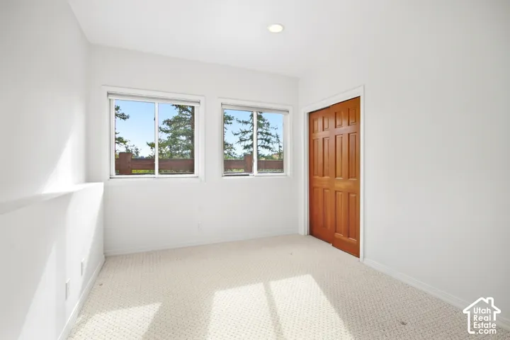 White walls, recessed ceiling lighting, light-toned patterned carpet, two windows, and a wood-paneled bifold closet door