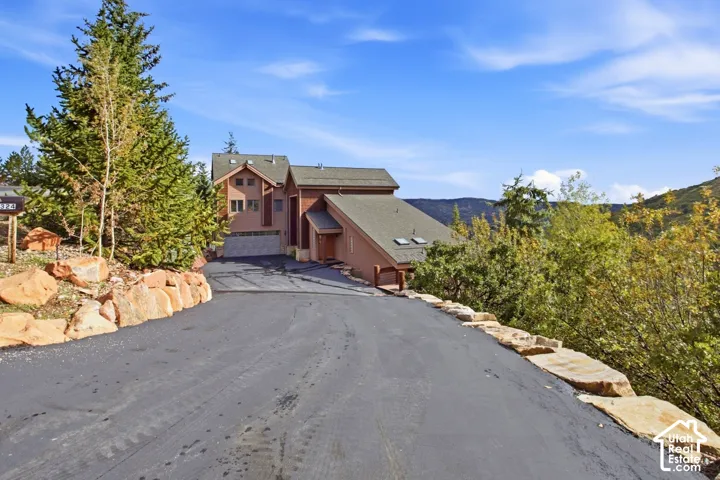 Paved driveway leading to a multi-level residence with a wood exterior, gabled roof, and visible skylights