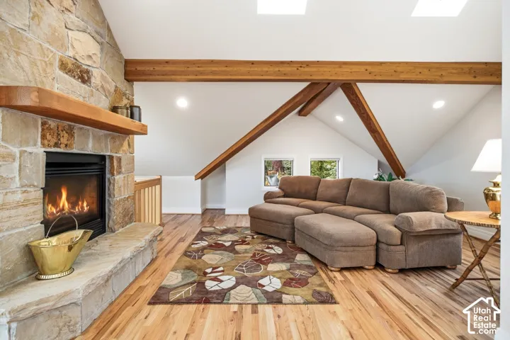 Stone-clad fireplace with wood mantle, exposed wood ceiling beams, vaulted ceilings, skylights, and wood-finish flooring