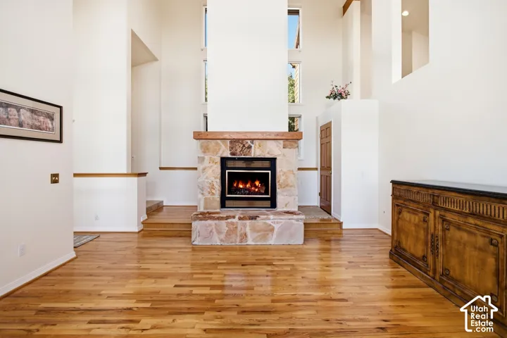 Stone-clad fireplace with wood mantle, high ceilings, large windows, and wood-finish flooring