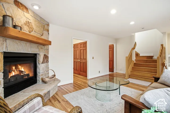 Stone-clad fireplace with a wood mantel, wood-finish flooring, recessed lighting, and a wood staircase with a matching railing