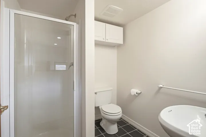 White-framed shower enclosure, pedestal sink, wall-mounted cabinetry, and dark-toned floor tiling