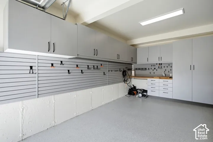 Coated concrete floor, extensive overhead cabinetry, built-in slatwall organization, integrated workbench with countertop, and drawer storage