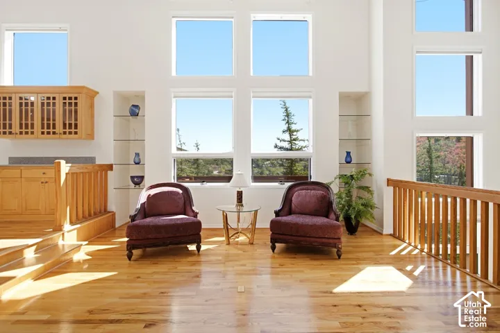 Two-story ceiling, light wood-finish flooring, built-in cabinetry with glass panels, integrated shelving, and large multi-pane windows