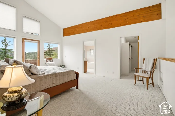 Vaulted ceiling with exposed wood beam, large windows with pleated shades, light-colored carpeting, and a built-in railing
