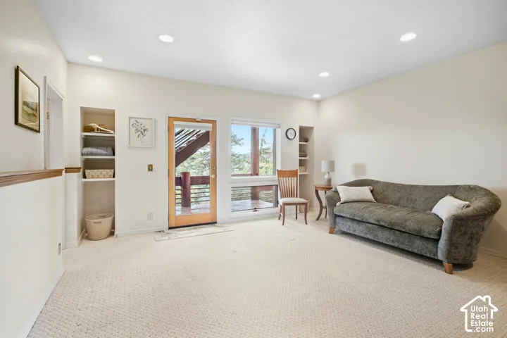 Plush carpet flooring, recessed ceiling lighting, built-in shelving, glass door access to an exterior balcony, and large windows