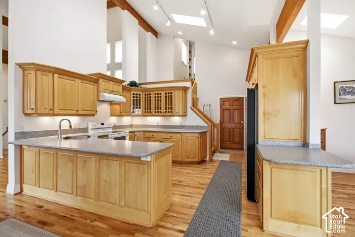 Open-concept kitchen with light wood cabinetry, stone-finish countertops, wood-finish flooring, exposed wood ceiling beams, and vaulted ceilings