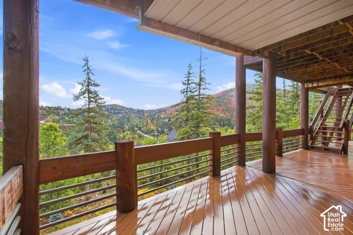 Expansive outdoor deck with wood-finish flooring, sturdy log columns, horizontal metal railing, and a visible staircase