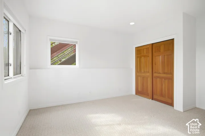 Recessed lighting, wood panel bi-fold doors, two windows, and light-toned carpet flooring