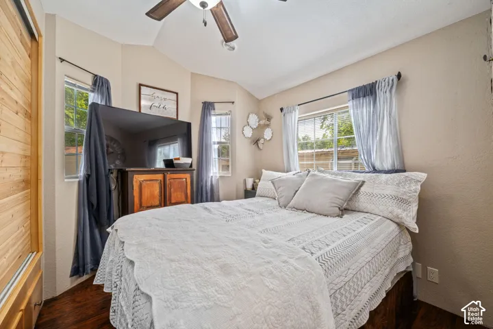 Vaulted ceiling with a ceiling fan, recessed window alcoves, wood-finish flooring, multiple windows