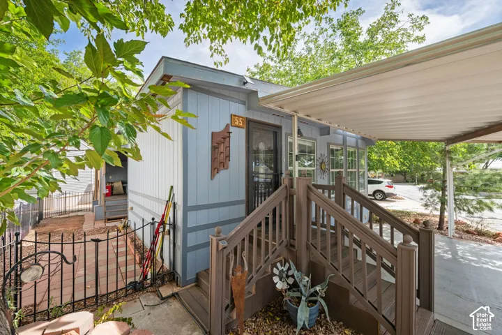 Covered carport with a light-colored roof, exterior siding, and a partially covered porch featuring wood-finish railings