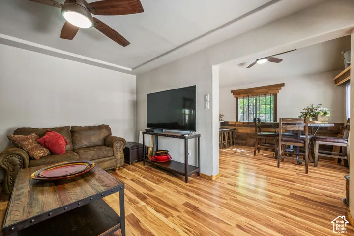 Wood-finish flooring throughout, featuring a recessed ceiling, a wood-finish ceiling fan with integrated lighting, and a wood-paneled accent wall in the dining area