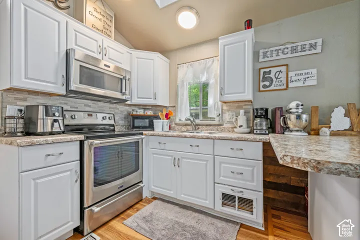 White cabinetry, stainless steel appliances, stone-look countertops, tiled backsplash, and wood-finish flooring