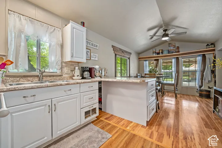 Kitchen featuring white cabinetry, wood-finish flooring, vaulted ceiling, built-in shelving, and a ceiling fan