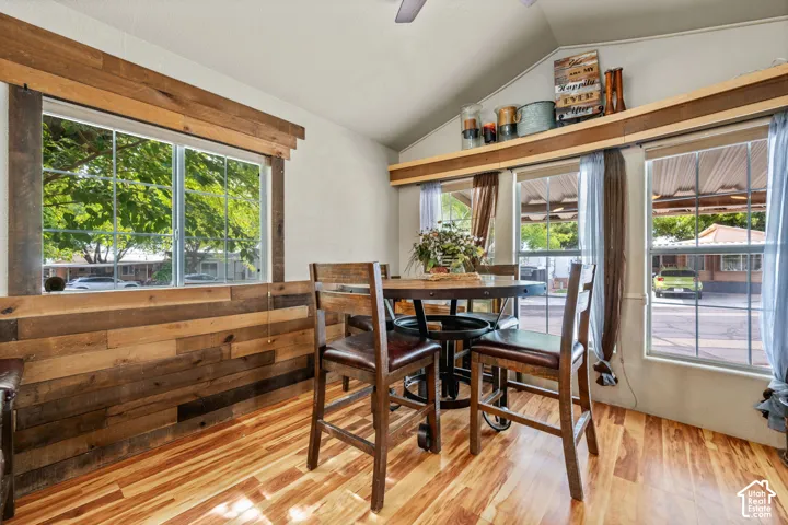 Vaulted ceiling with a wood-finish ceiling fan, wood-finish flooring, and wood-paneled accent wall