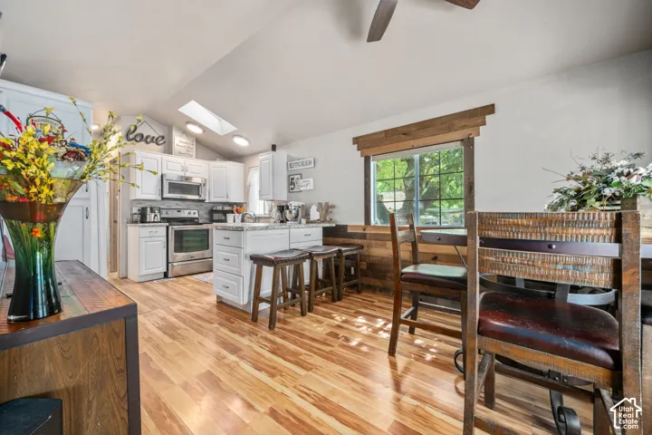Kitchen featuring white cabinetry, stainless steel appliances, a center island with seating, and wood-finish flooring