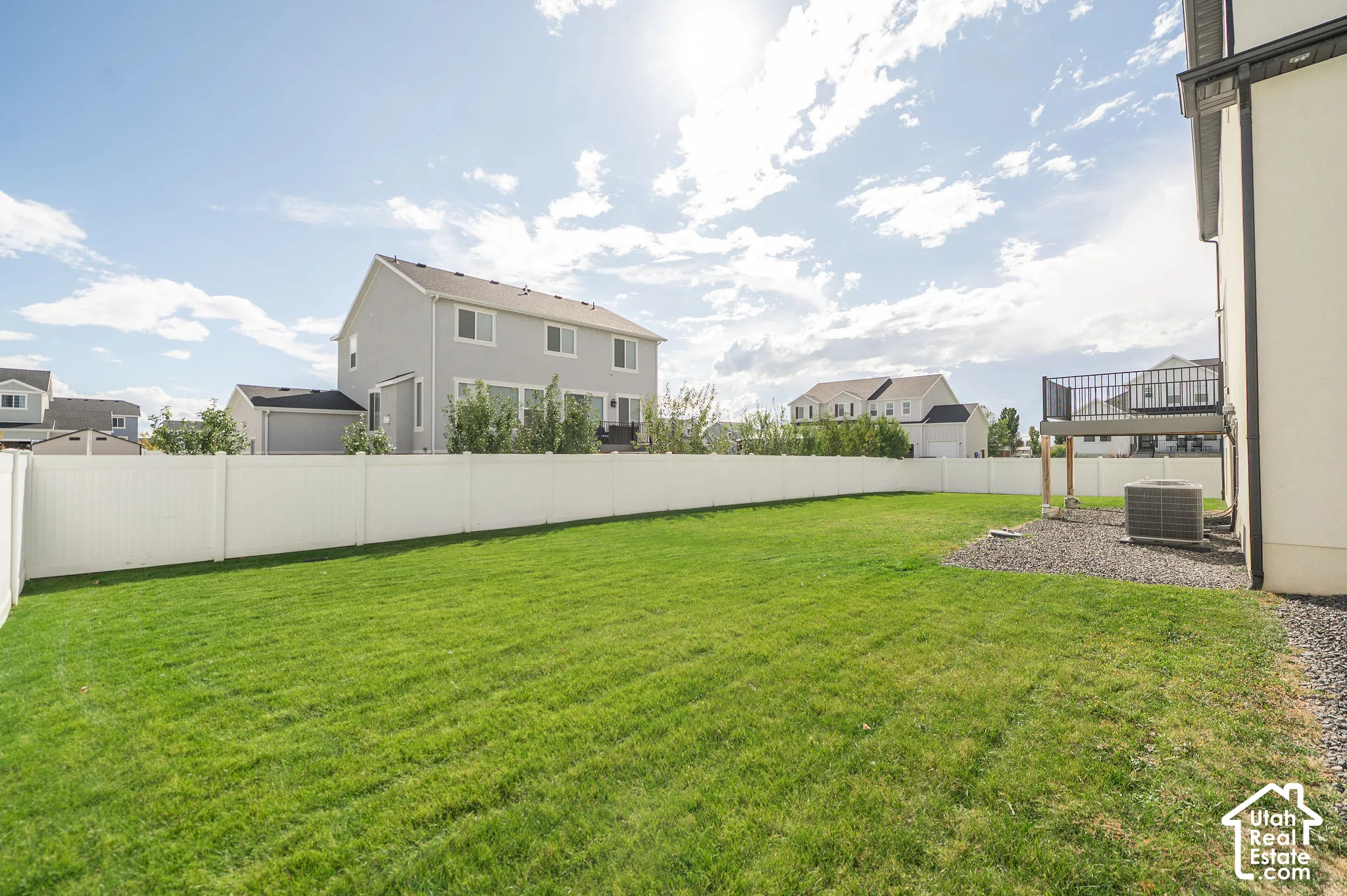 Expansive grassy lawn with a white privacy fence and a rear deck featuring black metal railings