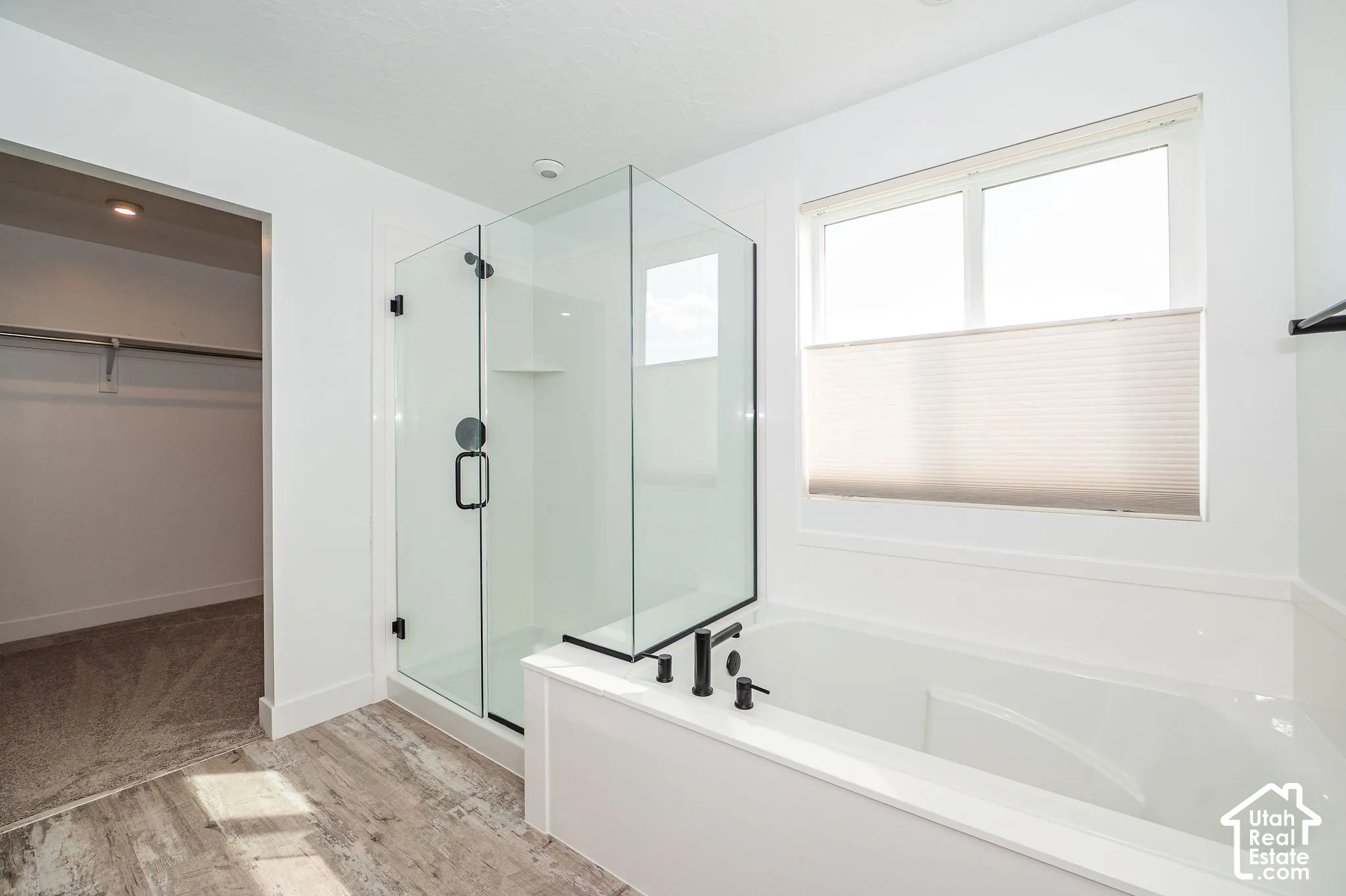 Glass-enclosed shower with matte black hardware, built-in shower niche, soaking tub with matte black fixtures, and wood-finish flooring in master
