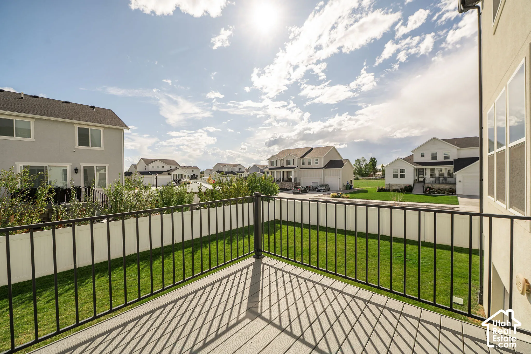 Outdoor deck with composite decking and black metal railing overlooking a fenced yard with green lawn