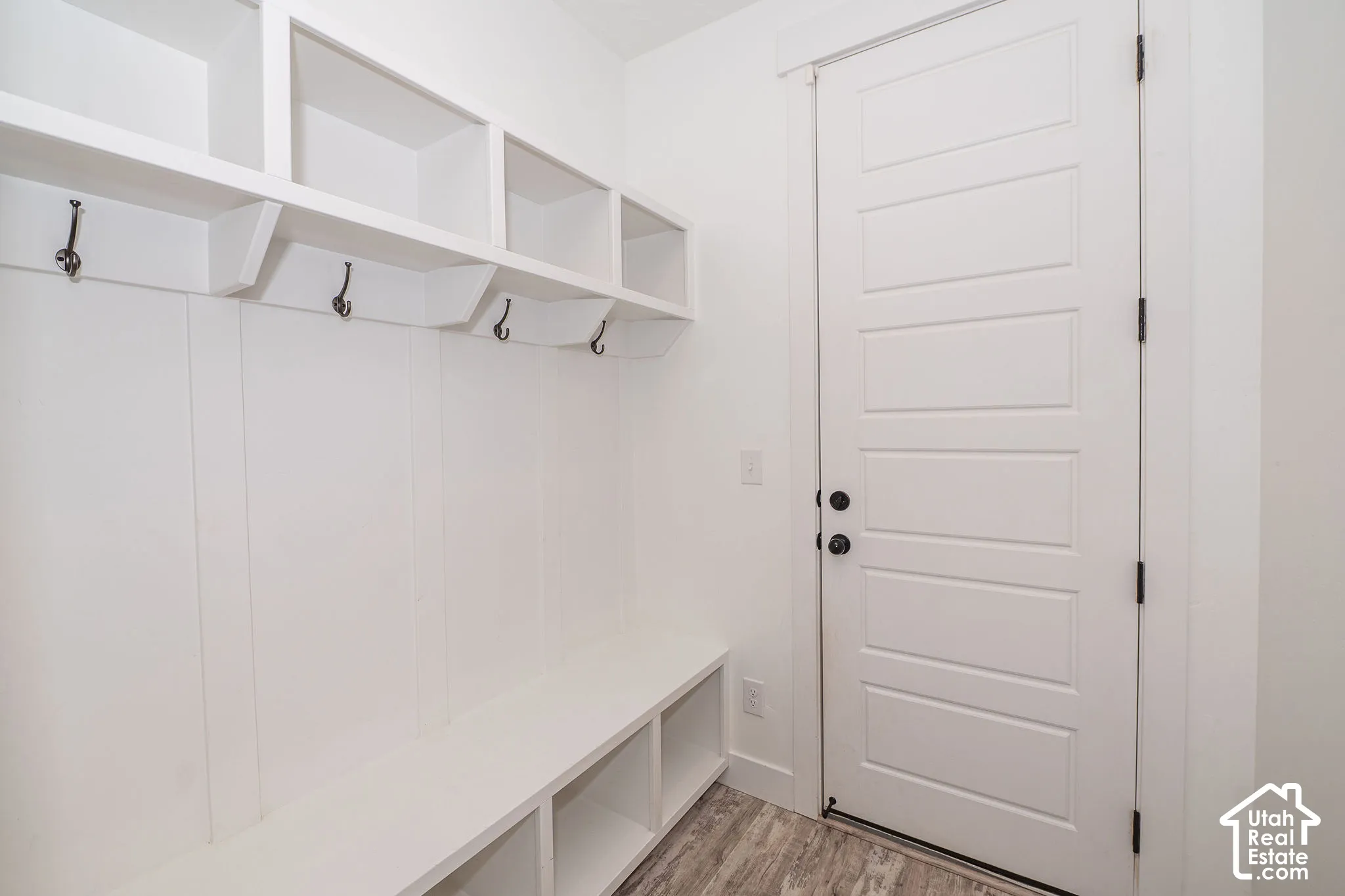 Built-in white storage bench with open shelving, wall hooks, and wood-finish flooring