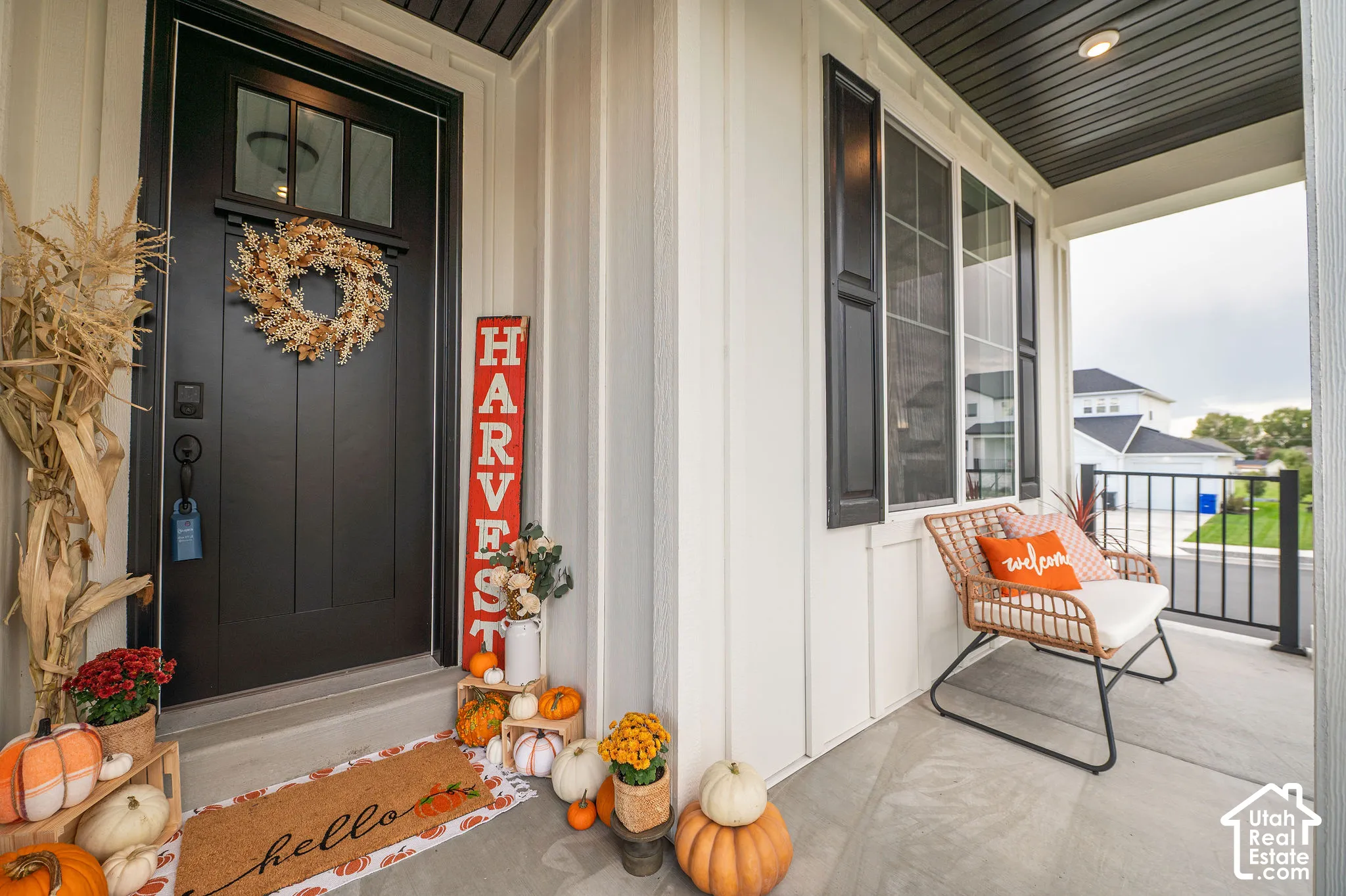 Covered front porch featuring white vertical siding, a black entry door with transom windows, and black exterior shutters