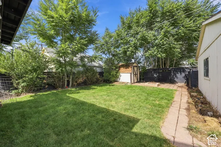 Expansive backyard featuring a lush lawn, mature trees, a paver pathway, and a storage shed