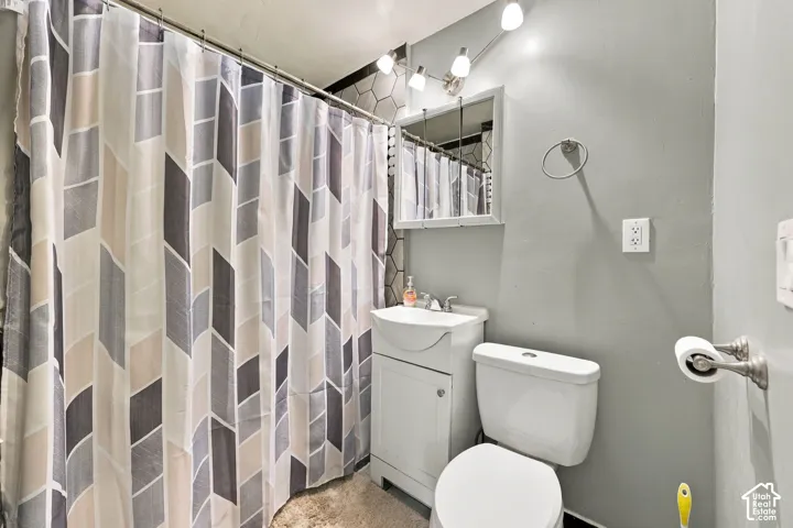 Bathroom featuring a shower with a patterned curtain, a vanity with an integrated sink, a wall-mounted medicine cabinet, a toilet, and brushed nickel fixtures