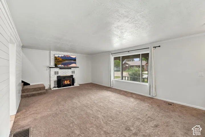 Carpeted living area featuring a white brick fireplace with a black insert, a large window, white shiplap accent wall, and crown molding
