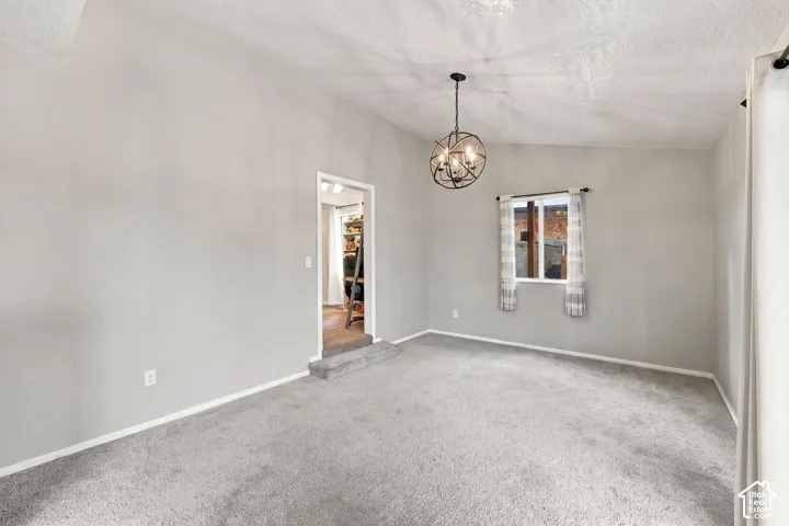 Light grey walls with textured ceiling and light grey carpeting, featuring a modern spherical chandelier and a window with white trim