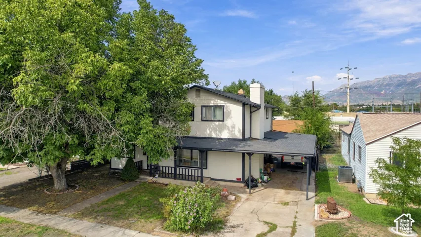 Two-story residence with a covered carport, prominent front-facing chimney, and a mature shade tree