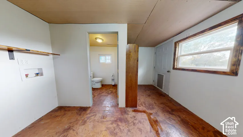 Utility area featuring wood-finish flooring, a wall-mounted shelf, and an exposed laundry hook-up