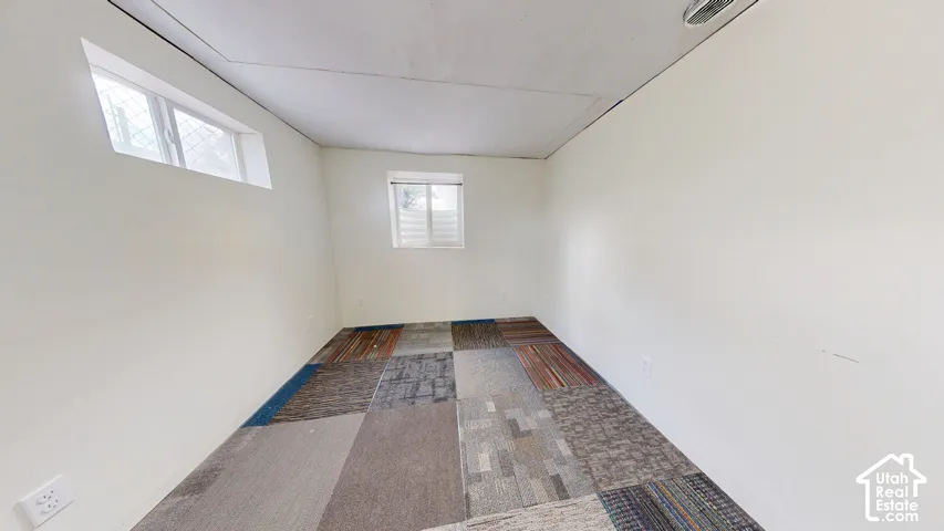 White painted walls, two windows, and multi-patterned carpet flooring