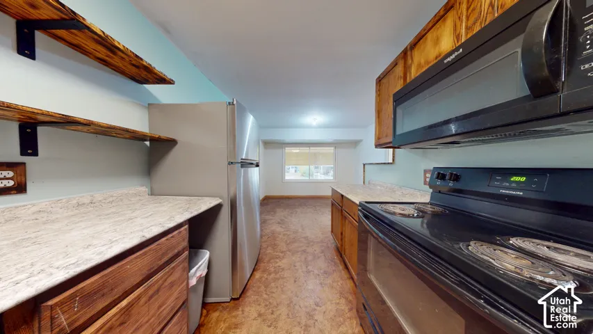 Kitchen featuring wood-finish flooring, wood cabinetry, stone-look countertops, stainless steel refrigerator, and a built-in microwave