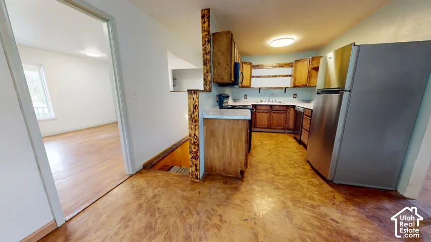 Wood-finish flooring throughout, stainless steel refrigerator, and wood cabinetry in the kitchen