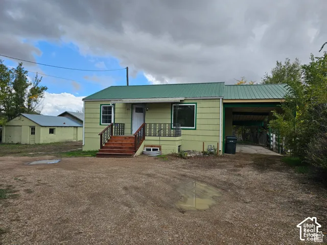 Light green exterior with a green metal roof, wood-finish porch, and a covered carport