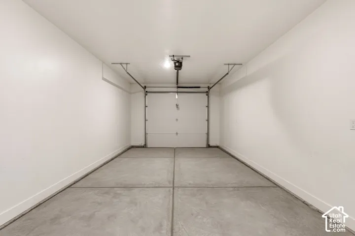 Concrete floor with dividing joints, white painted walls, white overhead garage door, and overhead lighting fixture