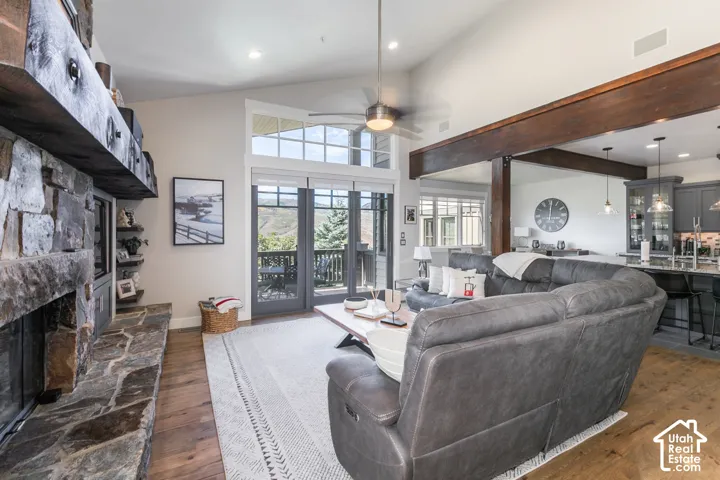 Vaulted ceilings with exposed wood beams, a stone-clad fireplace, wood-finish flooring, and double doors opening to a balcony