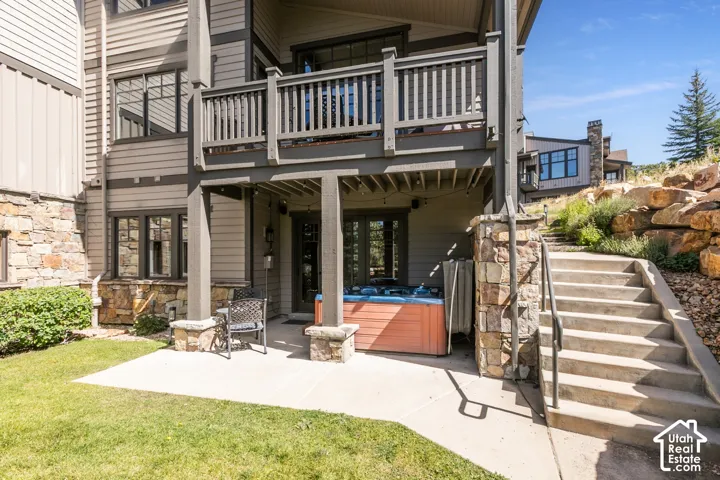 Exterior patio with an attached spa, concrete stairs with stone-clad pillars, and an upper-level balcony featuring wood railings