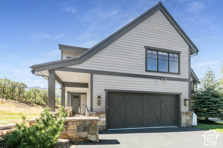 Contemporary exterior featuring horizontal siding, a covered entry porch with substantial columns, a two-car garage with cross-brace doors, stone veneer accents, and dark-framed windows