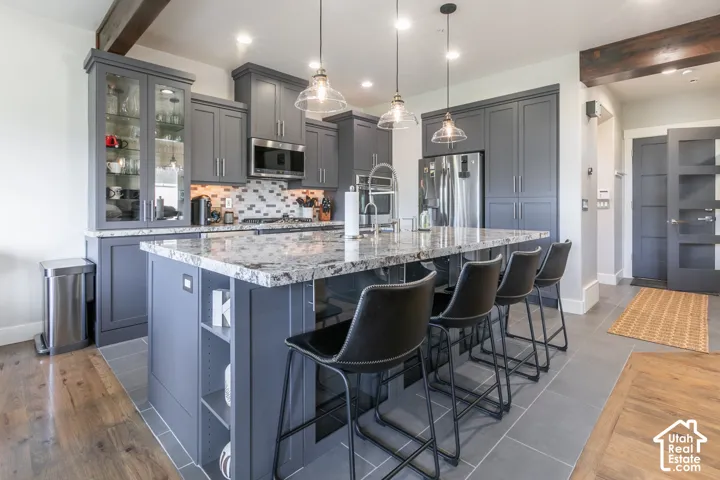 Kitchen featuring gray cabinetry, stainless steel appliances, a multi-tone tile backsplash, and a large island with a stone countertop