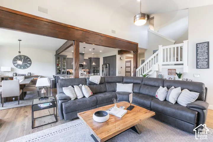Open-concept living area featuring wood-finish flooring, a vaulted ceiling, and a white staircase with a contemporary railing