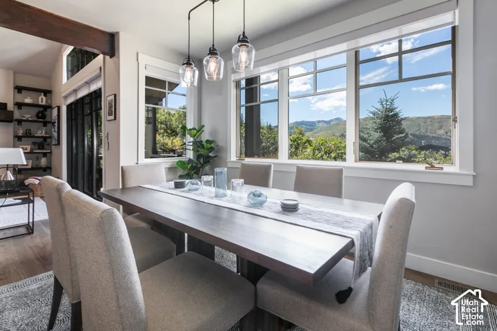 Wood-finish flooring, exposed wood beam, large windows with mountain scenery, glass pendant lighting, and built-in shelving