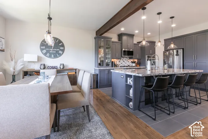 Open-concept kitchen and dining area featuring a prominent island with seating, pendant lighting, stainless steel appliances, and wood-finish flooring