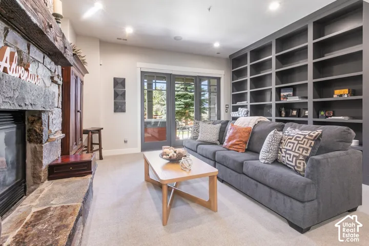 Stacked stone fireplace with a substantial timber mantel, built-in shelving, glass-paneled sliding doors, recessed lighting, and light-toned carpeting